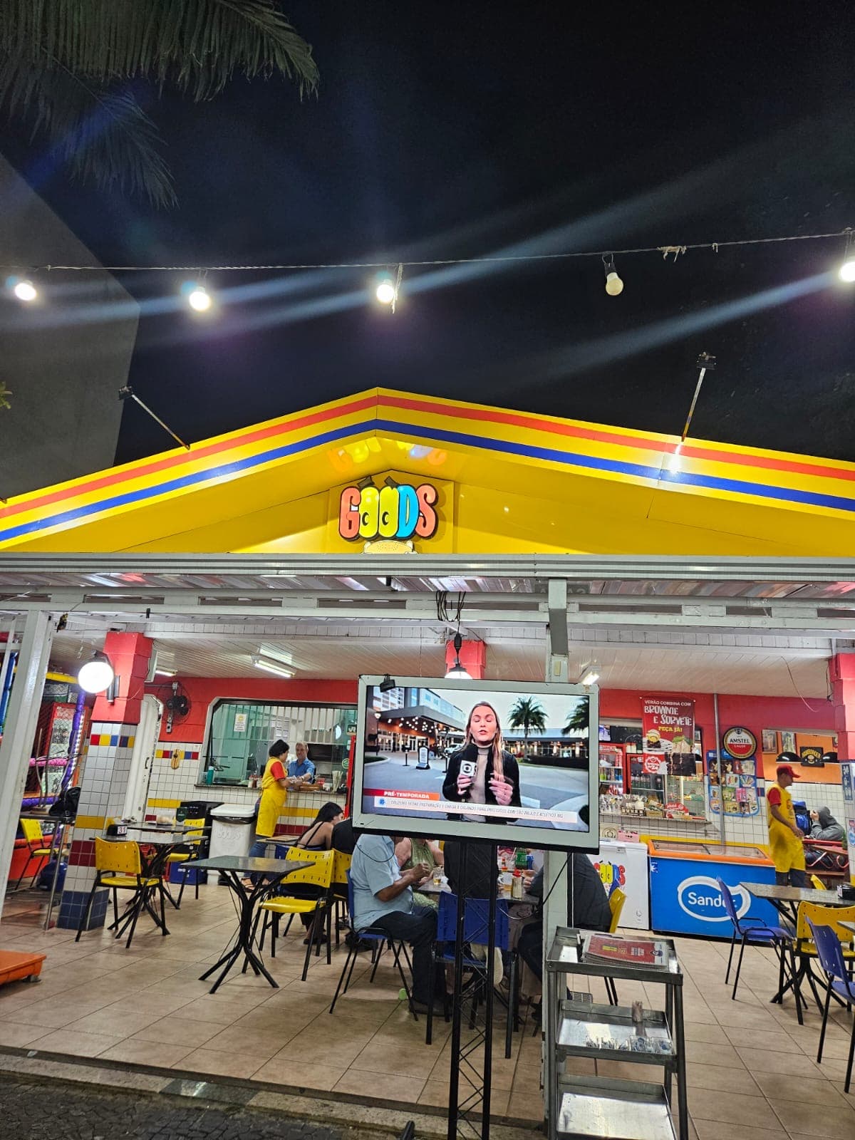 Fachada do Goods à noite, com o letreiro aceso no telhado amarelo