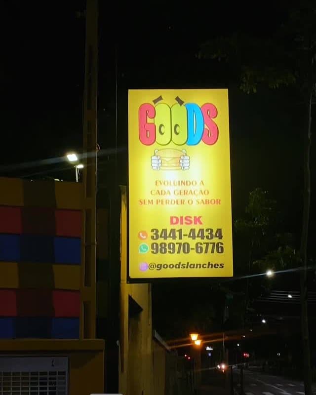A placa amarela do Goods acesa na rua à noite, com o telefone e o WhatsApp