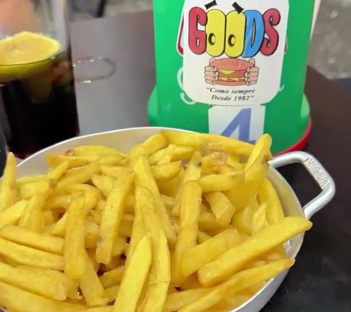 Porção de batata frita com o copo do Goods ao fundo